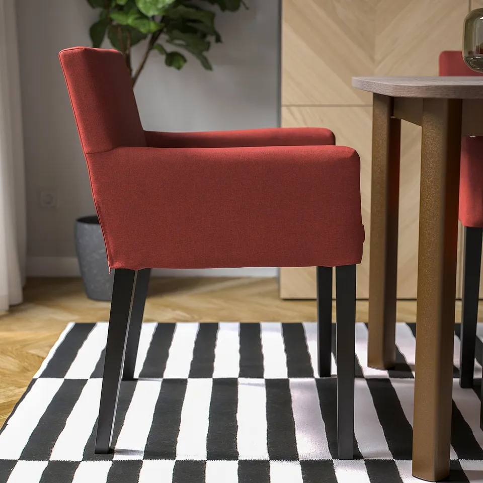 Red upholstered chair with armrests on striped rug near table.