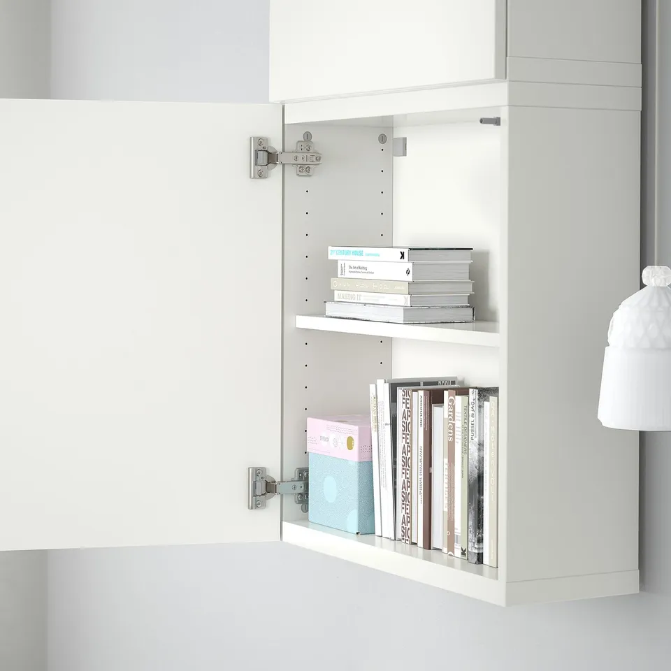 White cabinet with two shelves holding assorted books, mounted on wall with visible hinges.