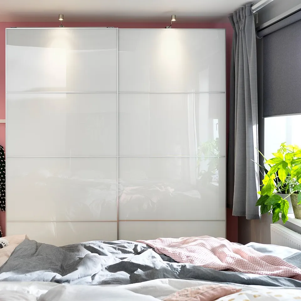 Bedroom with FÄRVIK white glass wardrobe, pink walls, grey curtains, and unmade bed featuring a teddy bear.
