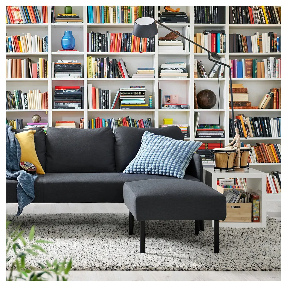 Cosy living room with GLOSTAD grey sofa and filled bookshelf, adorned with colourful pillows.