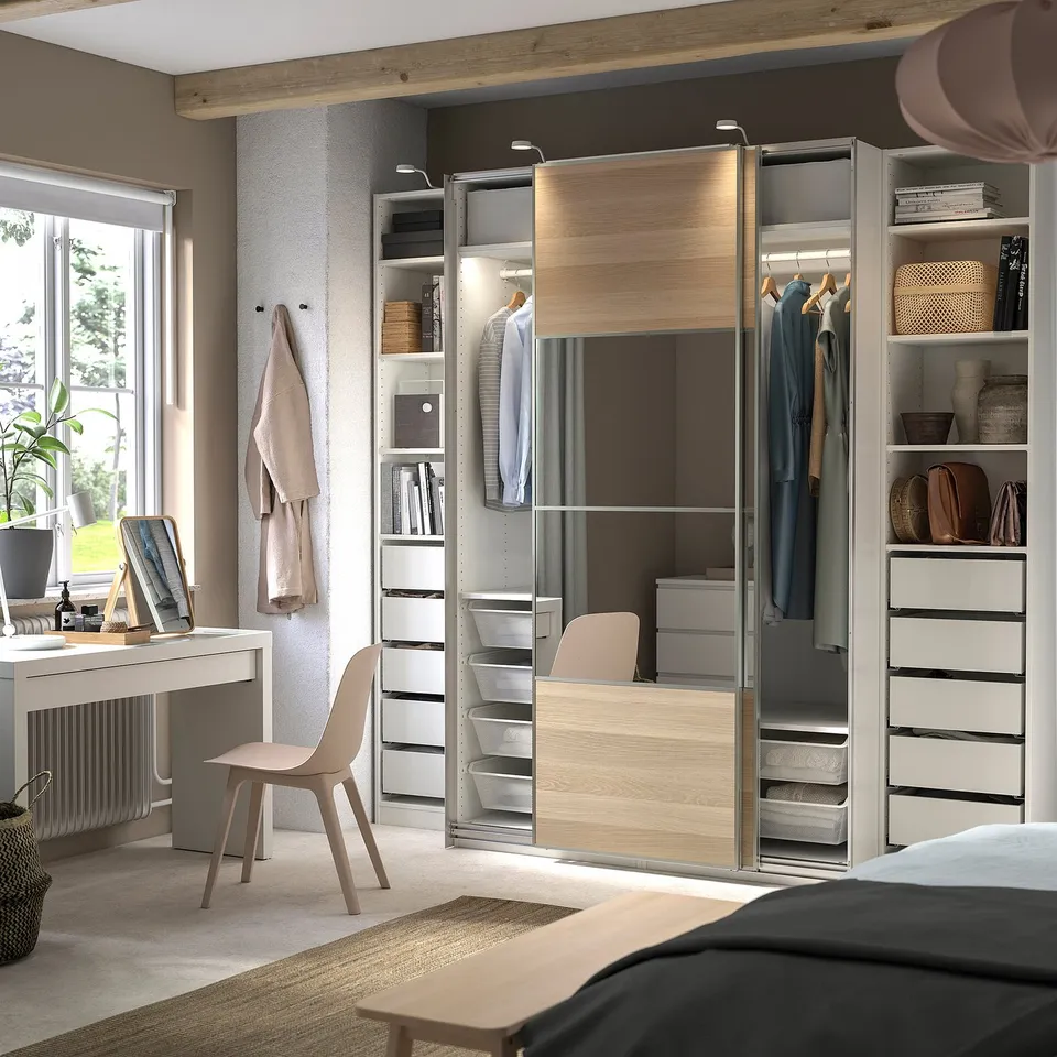 A modern bedroom with a beige PAX wardrobe and a light desk near a window.