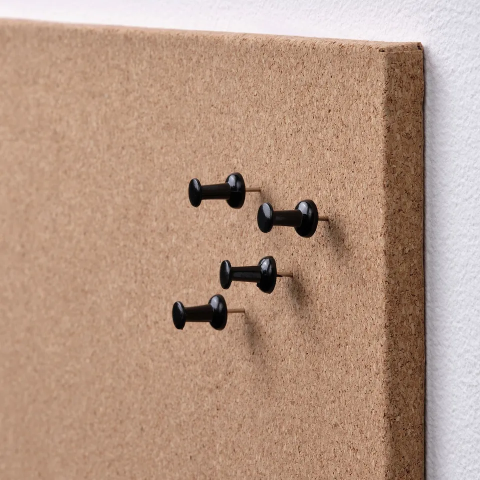 Cork memo board with black pushpins on a wall. Four pins are visible, evenly spaced.