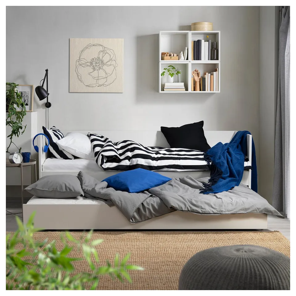 Cosy bedroom with VIHALS day-bed, striped cushions, shelves, grey rug, plant. Minimalist design.