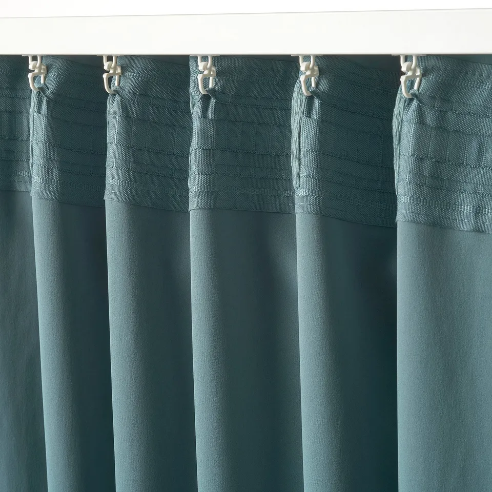 Dark grey-turquoise MAJGULL curtains hang from silver hooks, featuring room-darkening fabric for privacy and light control.