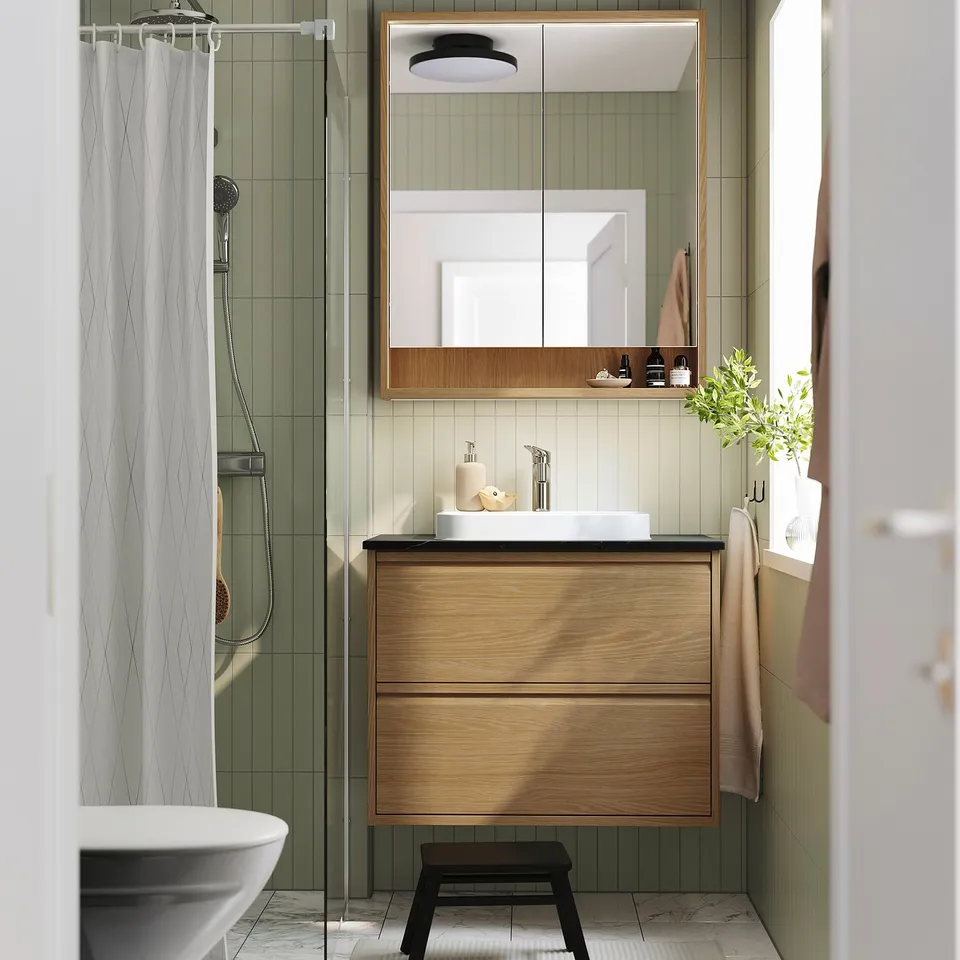 Modern oak vanity with marble basin, glass shower, green tiles, black stool