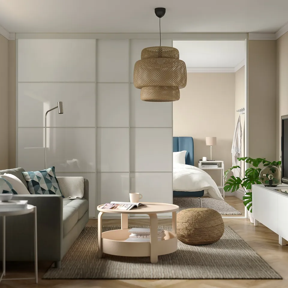 Modern living room with grey sofa, blue accents, wooden coffee table, teacup, magazine, woven stool, glass door, bright, neutral colours.