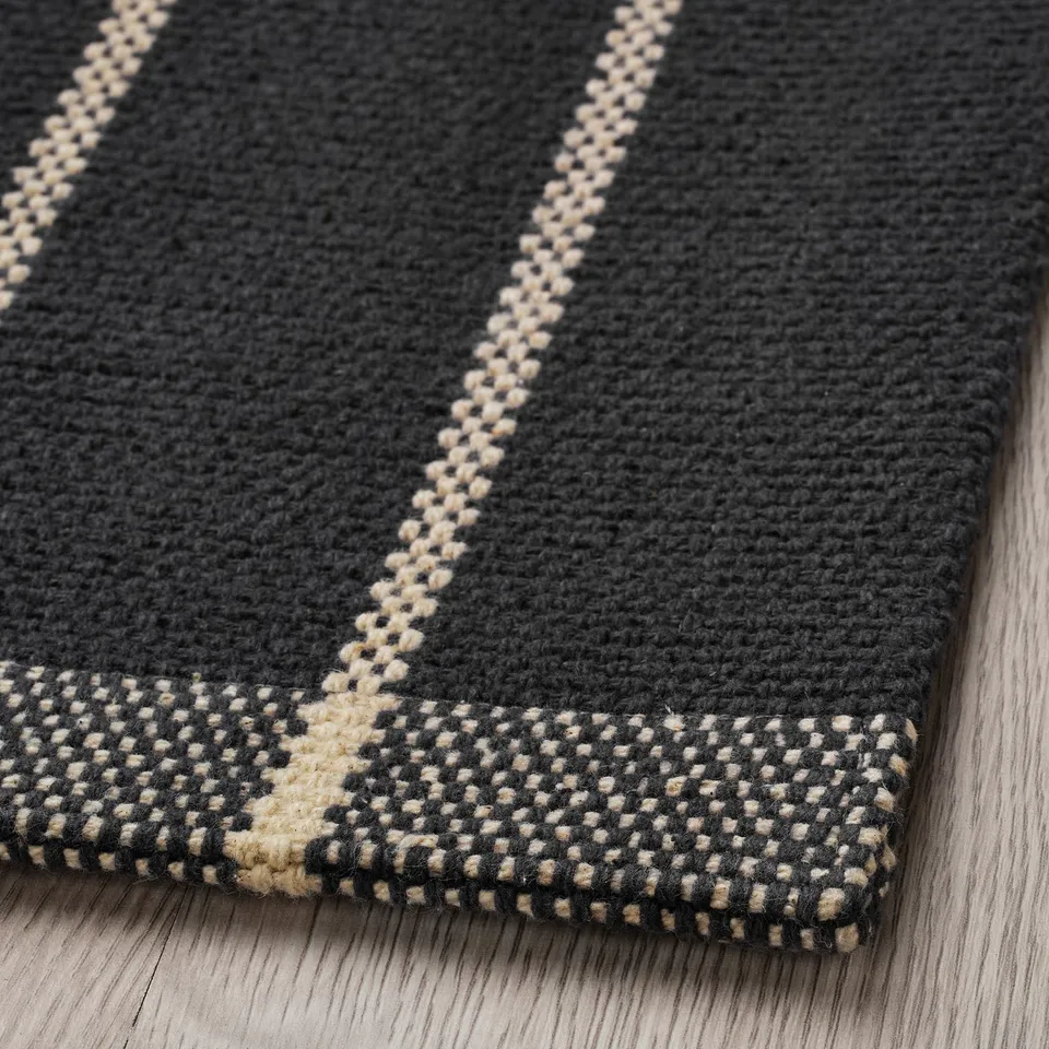 Plot of dark grey woven rug with off-white stripe pattern on wooden floor.